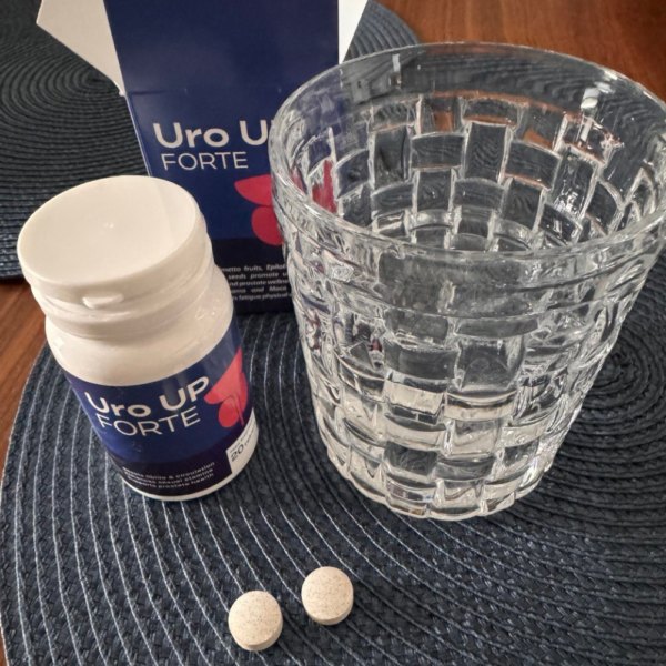 Flacone e scatola blu di Uro UP Forte con due compresse e un bicchiere d'acqua